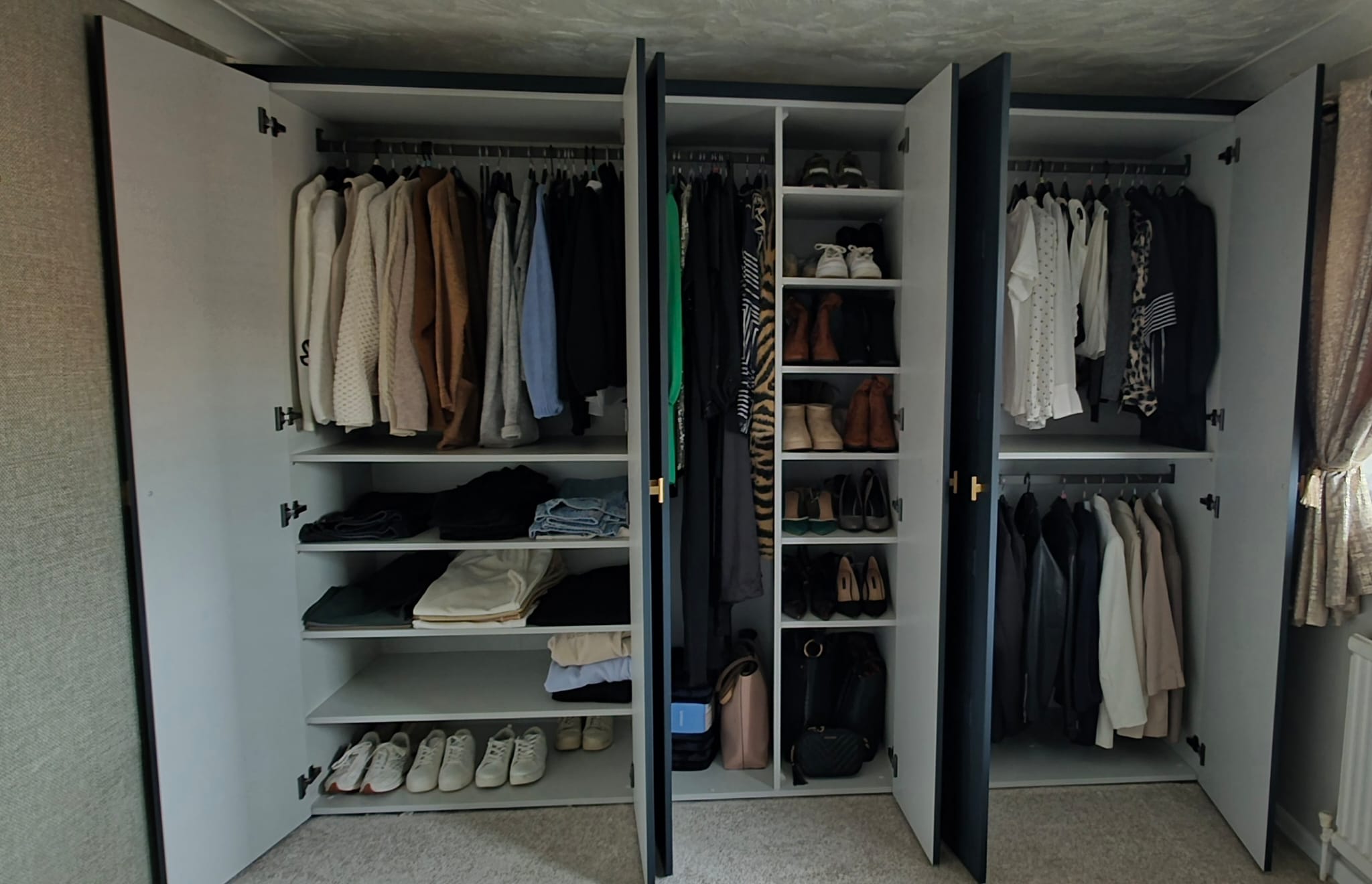 Built-in wardrobe with dark doors open to show hanging rails, shelves and shoe storage