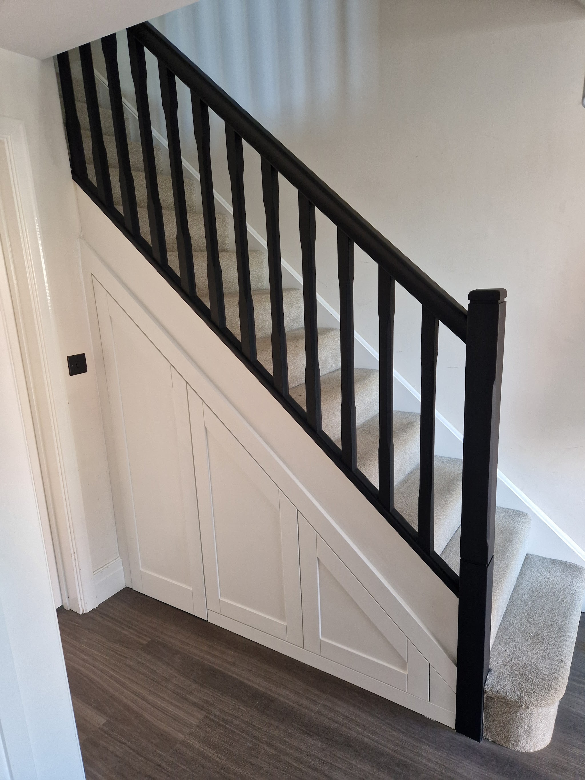 Panelled understairs storage below a black painted balustrade